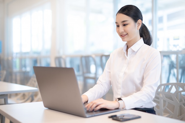 Young Asian business girl working with laptop in coffee shop cafe.