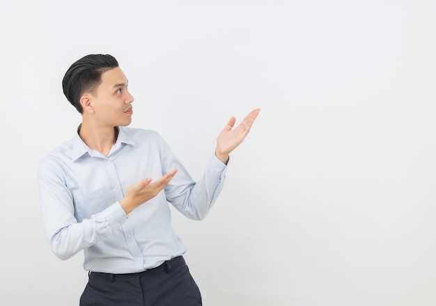 Young asian business man with blue shirt pointing to the side with a hand to present a product or an idea isolated on white