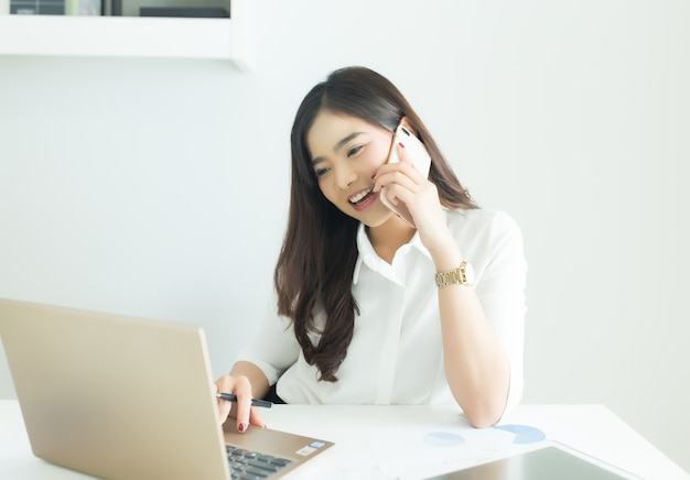 Young asian business woman talking on the mobile phone and smiling at office 