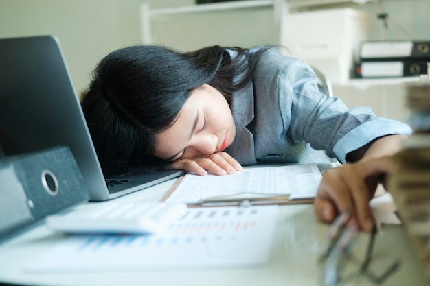 Young asian Business woman tired woman sleeping on desk with laptop at workplace alone