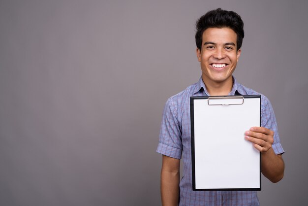 Photo young asian businessman holding clipboard against gray wall