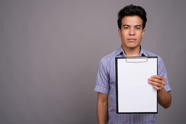 young Asian businessman holding clipboard against gray wall