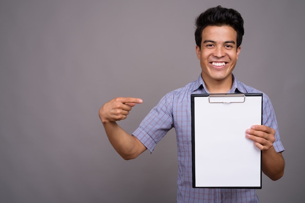 young Asian businessman holding clipboard against gray wall