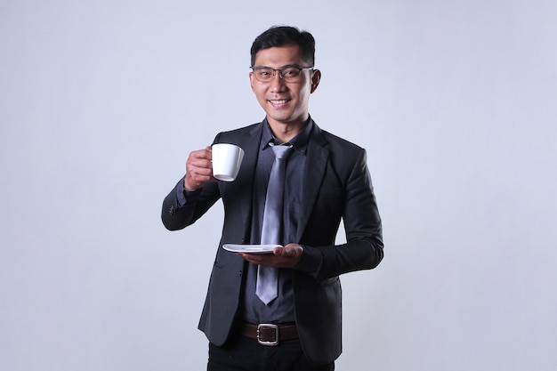 A young Asian businessman smiling and holding a cup of coffee