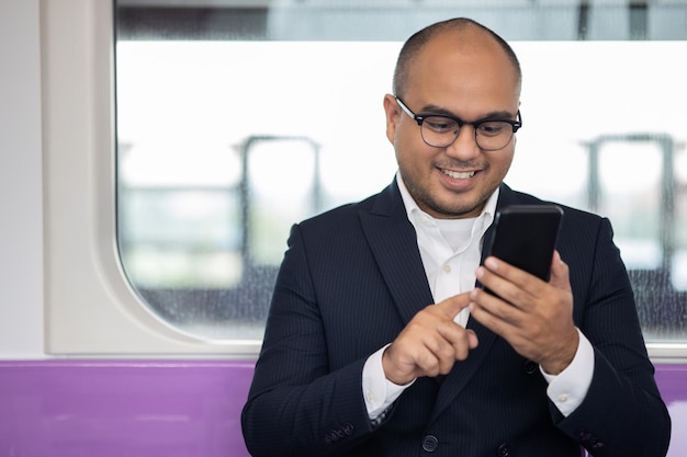 Young asian businessman using smartphone standing in skytrain. Businessman in urban city travel by sky train.