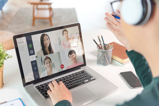 Young Asian businessman wear headphones working remotely from home and virtual video conference meeting with colleagues business people. social distancing at home office concept.