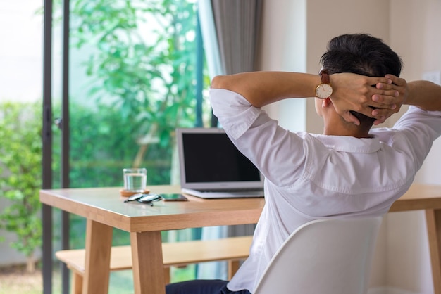 Young asian businessman wearing white shirt sitting at your desk Clasp your hands on the back of your head at home suffering from headache desperate and stressed because pain and migraine