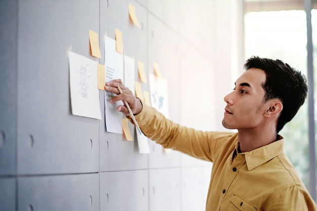 Young Asian Businessman Working in Office Meeting Room. Concentrate on Document Note at the Wall. Man Analyzing Data Plans and Project