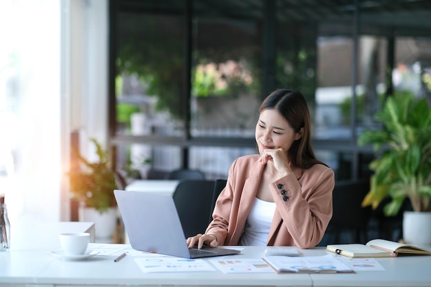 Young asian businesswoman beautiful charming smiling and using laptop computer in office