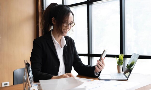 Young asian businesswoman beautiful charming smiling and using on mobile phone in the office