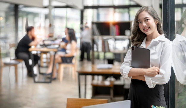 Young Asian businesswoman looking at camera holding tablet standing at office