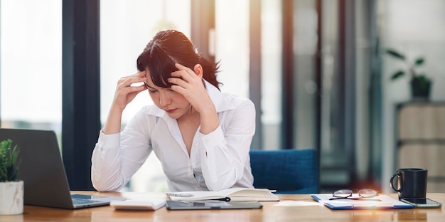 Young Asian businesswoman working on laptop computer stressed has a headache and thinks hard from work at the office