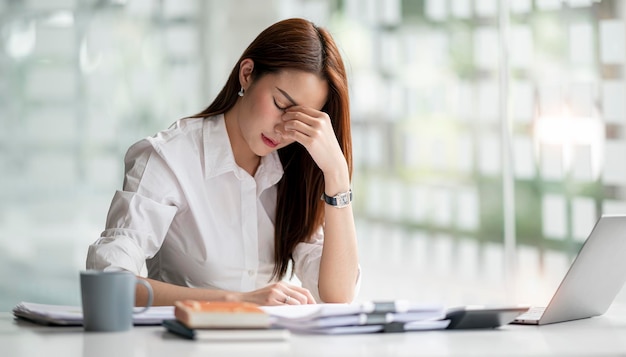 Young Asian businesswoman working on laptop computer stressed has a headache and thinks hard from work at the office