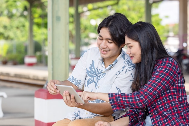 Young asian couple backpacker using tablet for find destination trip at railway station