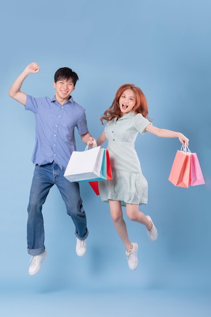 Young Asian couple carrying shopping bag on blue background