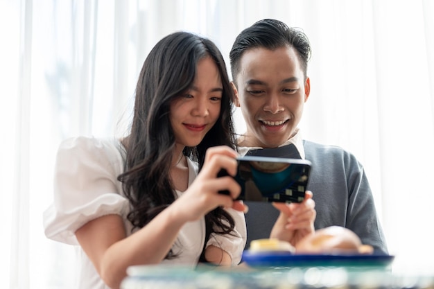 Young Asian couple having a date in a cafe having good time together and playing with smartphone