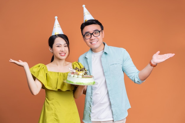 Young Asian couple holding birthday cake on background