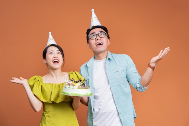 Young Asian couple holding birthday cake on background