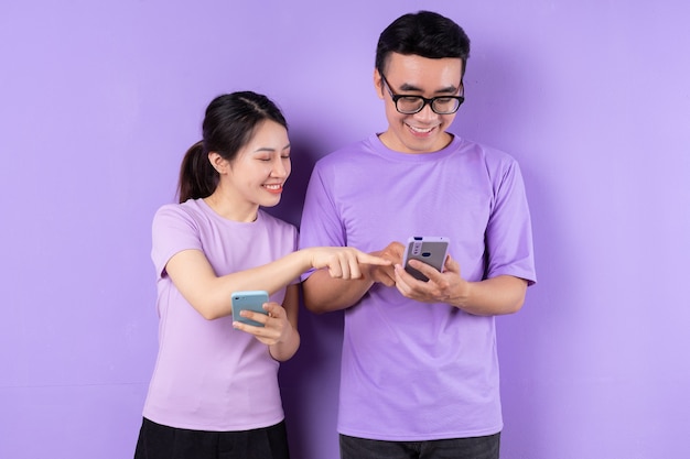 Young Asian couple using smartphone on purple background