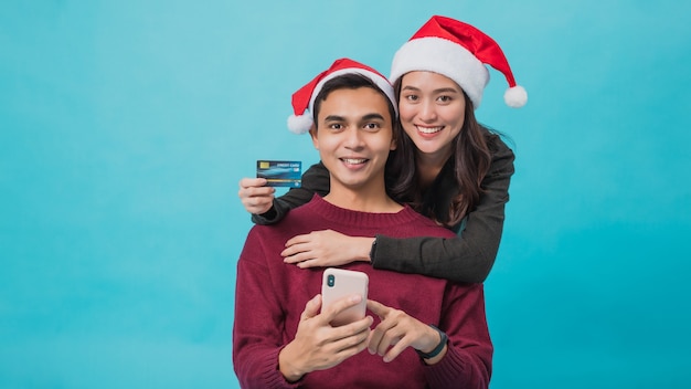 Young Asian couple wearing Santa Claus hats and shopping online with credit card and smartphone