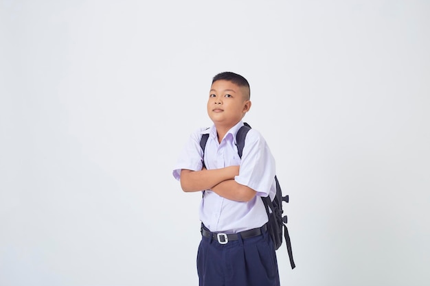 A young Asian cute boy standing in a Thai school uniform with a backpack bag and book on a white background banner