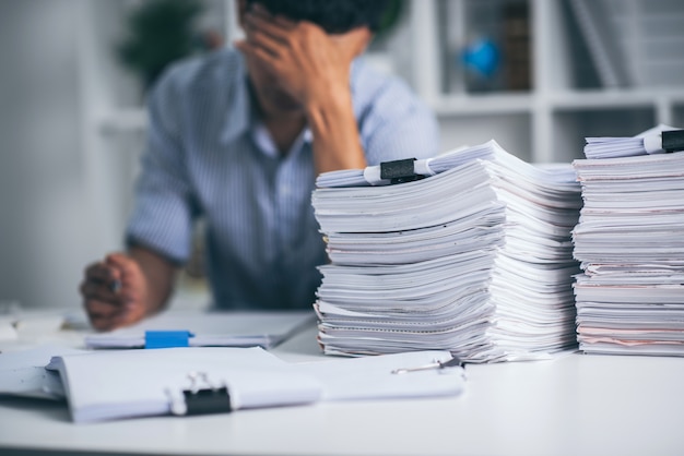 Young asian exhausted businesssman with messy desk and stack of papers, working busy, overwork.