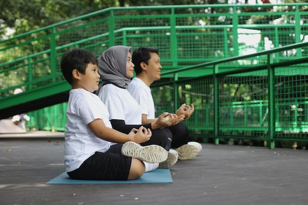 Young Asian family doing exercise in meditate yoga pose together at the greenery park. Healthy lifes