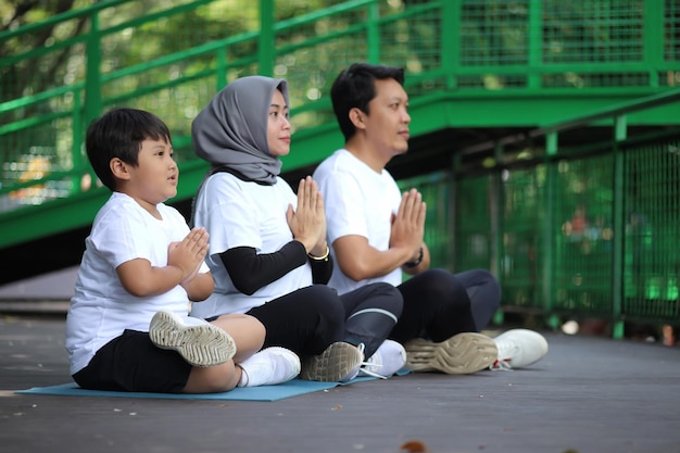 Young Asian family doing exercise in meditate yoga pose together at the greenery park. Healthy lifes