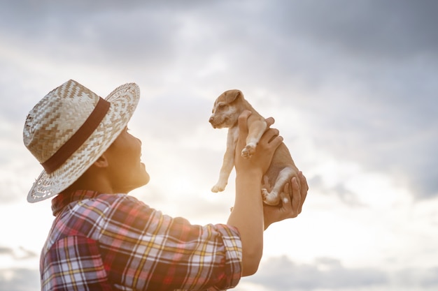 Young Asian farmer playing with his brown small pup in the evening after work