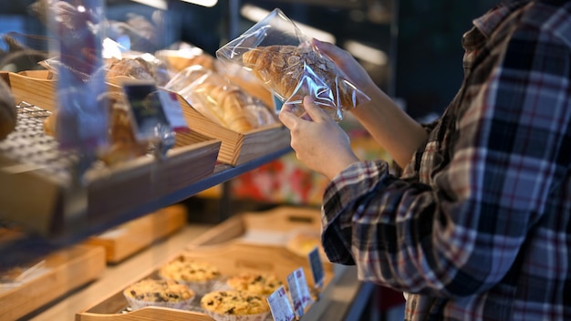 Young Asian female in the bakery shop looking and choosing a croissant cropped image