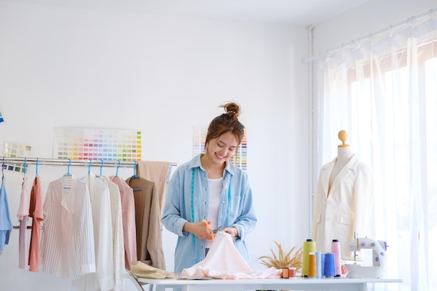 A young asian female fashion designer is cutting fabric and prepare a pattern for a new collection