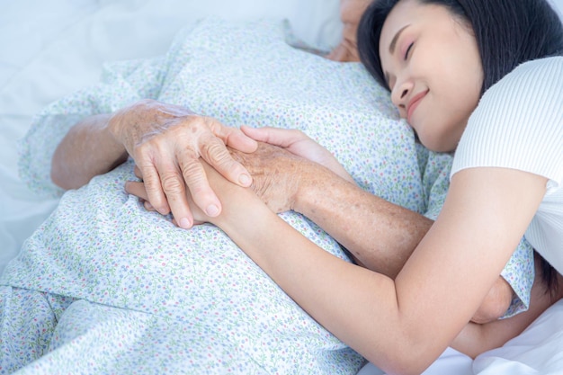 Young asian female holding hand elderly woman lying in hospital bed,  they feeling happy and smile.