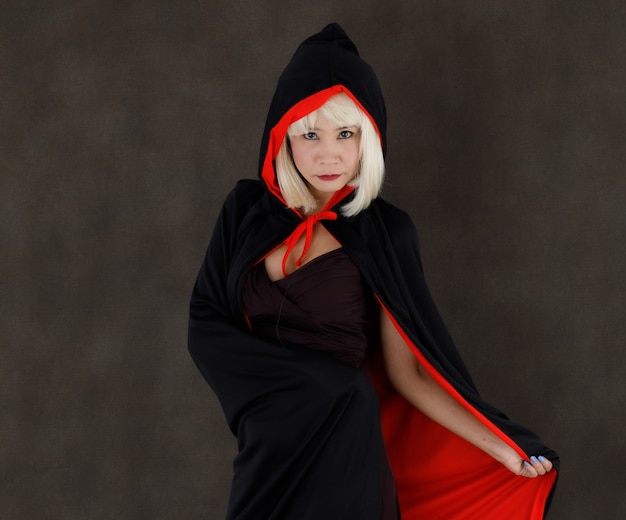 Photo young asian female with blond hair wearing black and red cloak with hood during halloween masquerade looking at camera