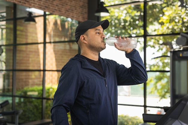 Young asian fitness man drinking fresh water while walking on the treadmill jogging indoor gym. Athlete workout running in the treadmill wearing sportswear.