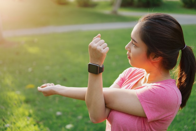 Young asian fitness woman wear smartwatch stretching arms, before exercise in park.