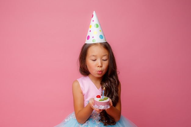 A young Asian girl blows out a candle on a pink  at a birthday party