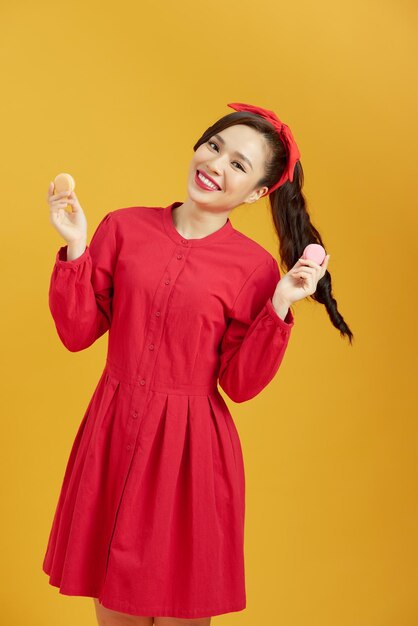 Young Asian girl over isolated yellow background holding colorful French macarons