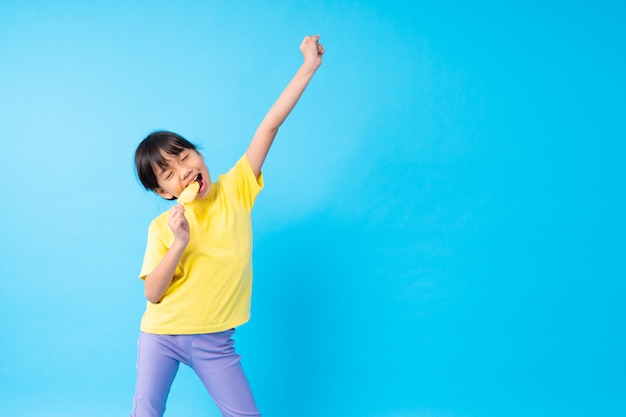 Young Asian girl kid eating ice cream and posting funny on blue