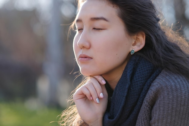 Young asian girl sitting in park with closed eyes and enjoying the moment