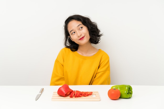 Young asian girl with vegetables in a table laughing and looking up