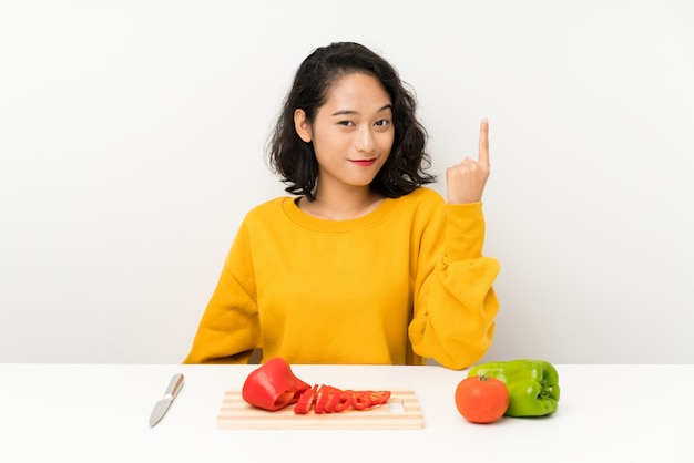 Young asian girl with vegetables in a table pointing with the index finger a great idea