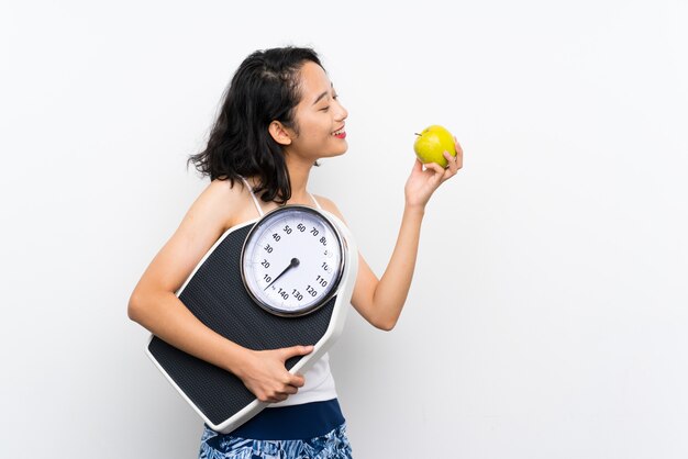 Young asian girl with weighing machine over isolated white wall