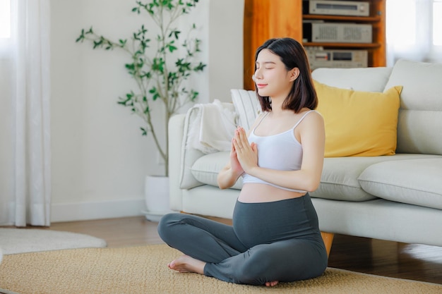 Young Asian happy pregnant woman is meditating while sitting in lotus position Family plan pregnancy motherhood people and expectation Meditating on maternity concept