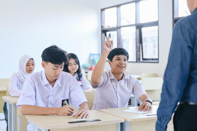 Young Asian high school student in uniform raising hands to answer question from the teacher at the