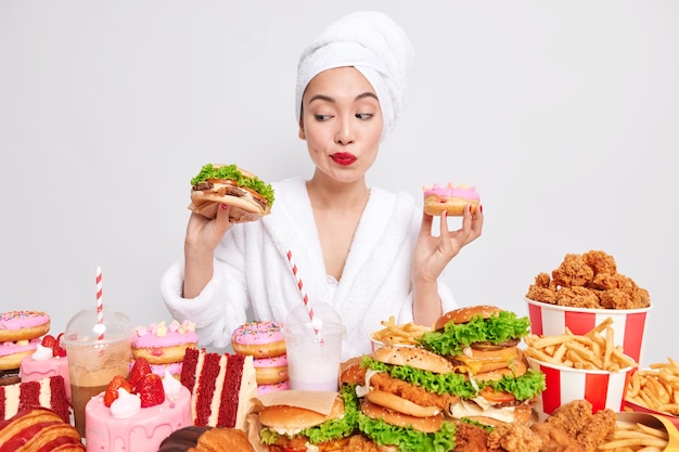 Young Asian lady doubts between a hamburger and a doughnut