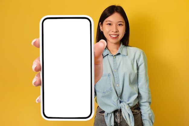 Young asian lady showing big smartphone with mockup promoting app or website advertising product or