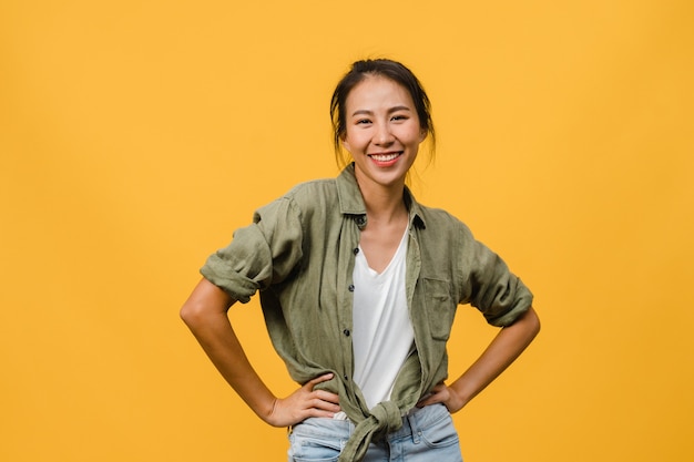 Young Asian lady with positive expression, smile broadly, dressed in casual clothing  over yellow wall. Happy adorable glad woman rejoices success. Facial expression concept.