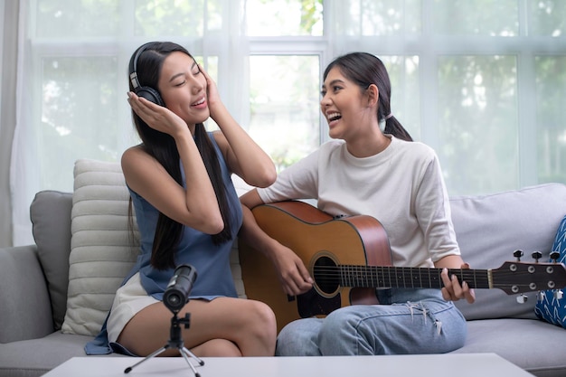 Young Asian lesbian couple blogger vlogger and online influencer recording musical video content playing guitar and singing at home LGBT lesbian couple performing and shooting clip for social media