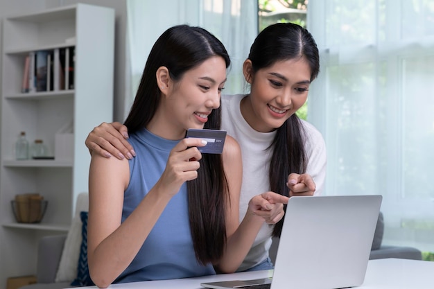 Young Asian lesbian couple holding credit card and using laptop computer LGBT lesbian businesswoman working at home Online shopping ecommerce internet banking spending money working from home concept