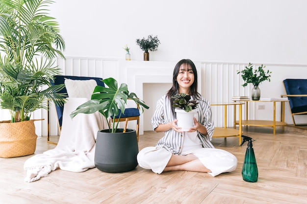 Young Asian long black hair woman holding a small house plant in the pot with care and smile sitting with a plant spray bottle Monstera and house plant lover at home The concept of plant care